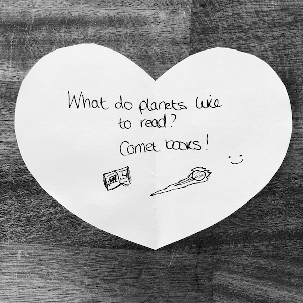 Space joke for kids: what do planets like to read? Comet books! Handwritten on a heart-shaped note.