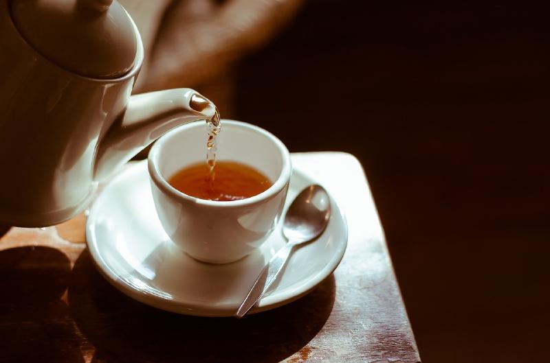 Pouring tea from a teapot into a white cup on a white saucer