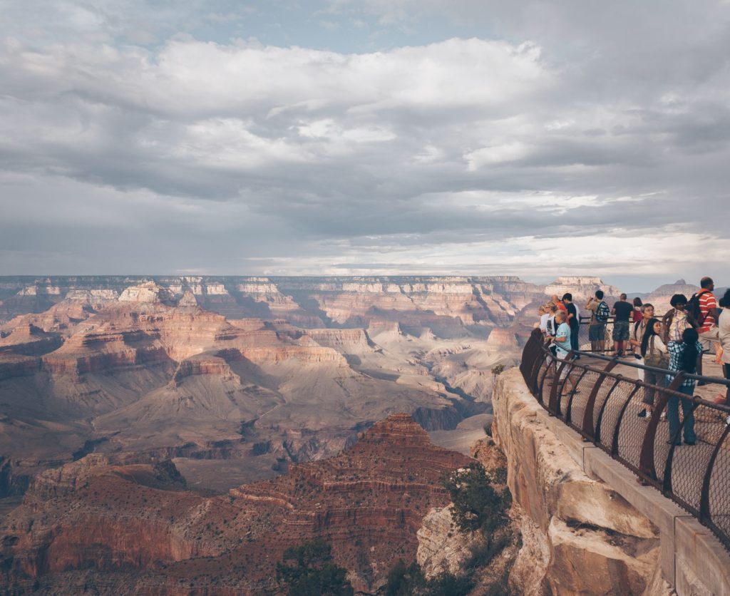 A group of people standing at a railing at the top of a cliff looking at a vista of the Grand Canyon