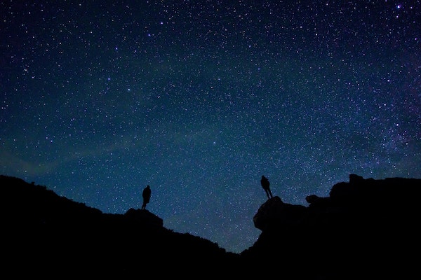 Two people standing on rocks silhouetted against a dark starry sky