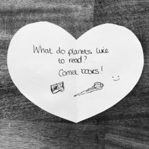 Space joke for kids: what do planets like to read? Comet books! Handwritten on a heart-shaped note.