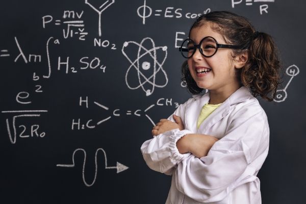 Girl with glasses laughing in front of blackboard with chemical formulae in white chalk