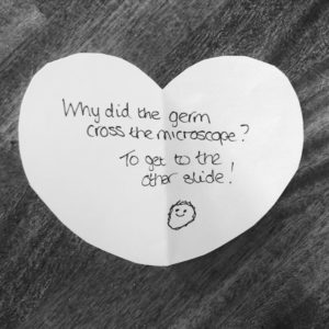 Biology joke for kids: Why did the germ cross the microscope? To get to the other slide! Handwritten on a heart-shaped note.