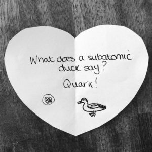Science joke for kids on a white paper heart: What does a subatomic duck say? Quark!
