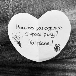 Science joke for kids on a white paper heart: How do you organise a space party? You planet!