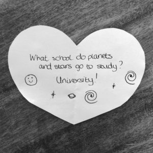 Science joke for kids on a white paper heart: What school do planets and stars go to study? University!