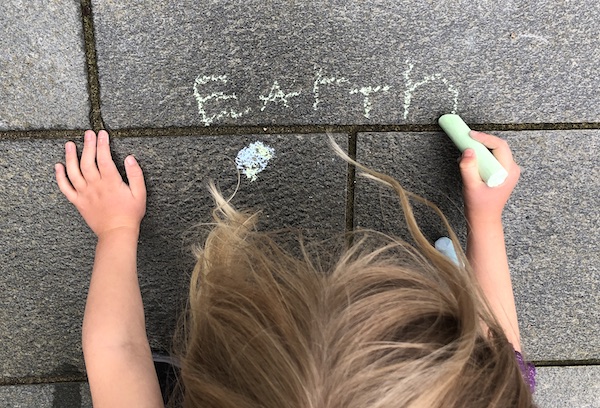 Child writing the name Earth in chalk while measuring the distances to planets in the Solar System to scale